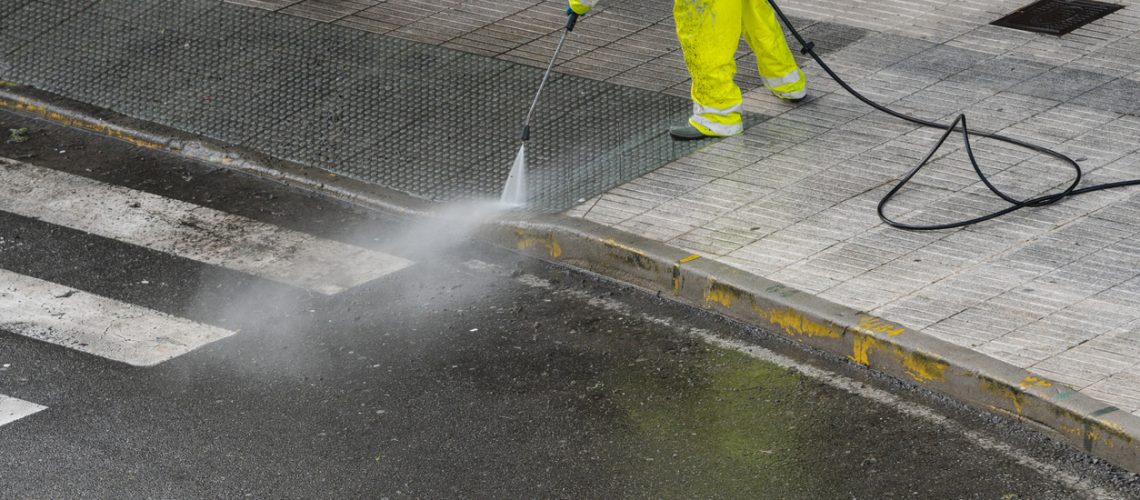 Worker cleaning the sidewalk with pressurized water